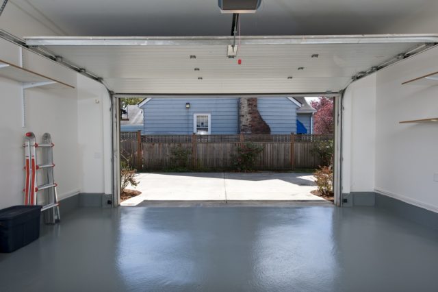 Garage floor covered in epoxy paint with door open showing house next door.